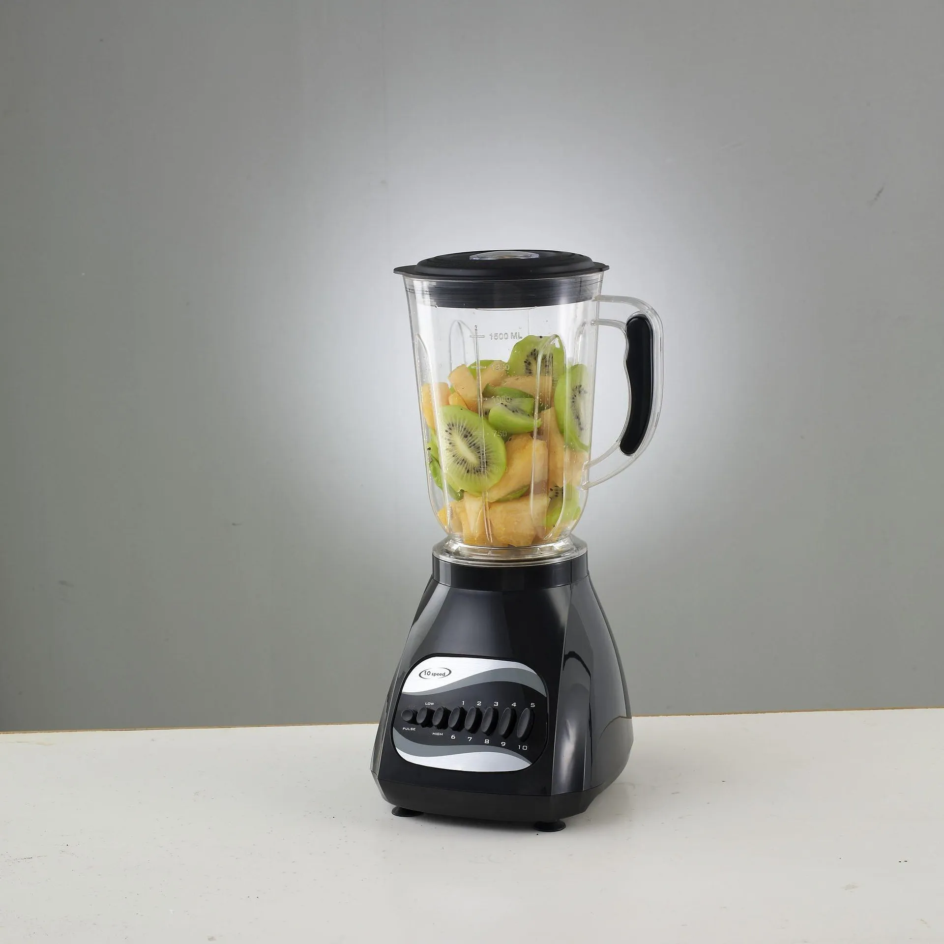 A black countertop blender with a clear jar filled with sliced kiwi and melon against a gray background