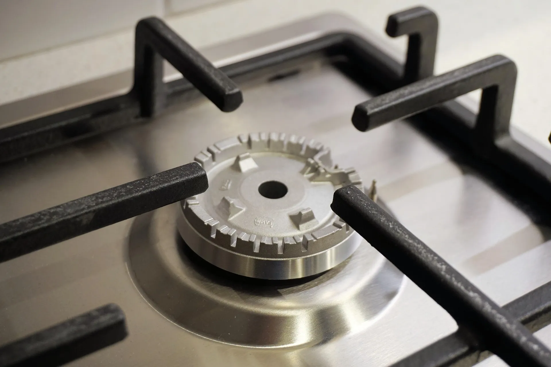 A close-up of a gas stove burner with black cast iron grates on a stainless steel cooktop