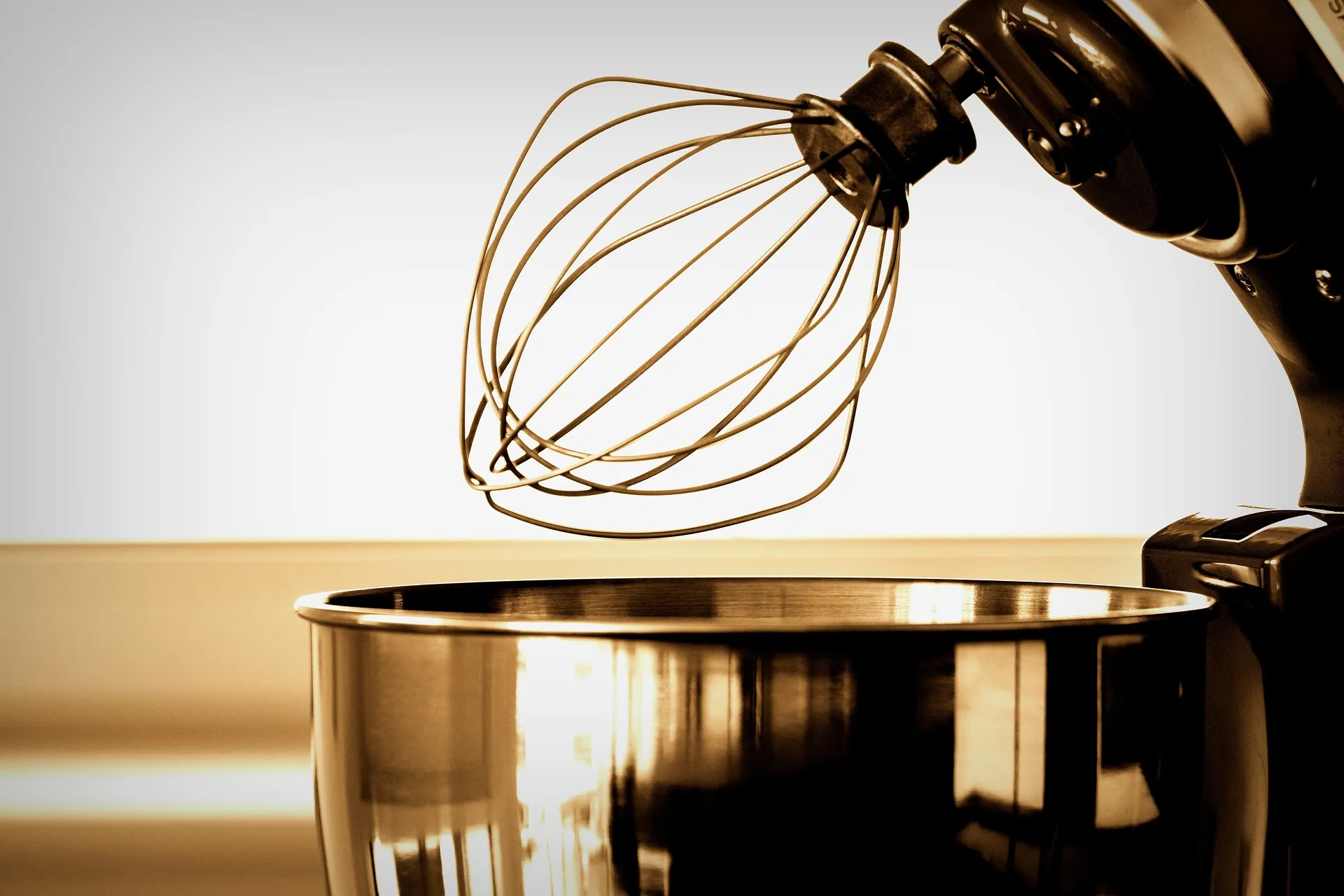 A sepia-toned photo of a stand mixer whisk above a stainless steel mixing bowl