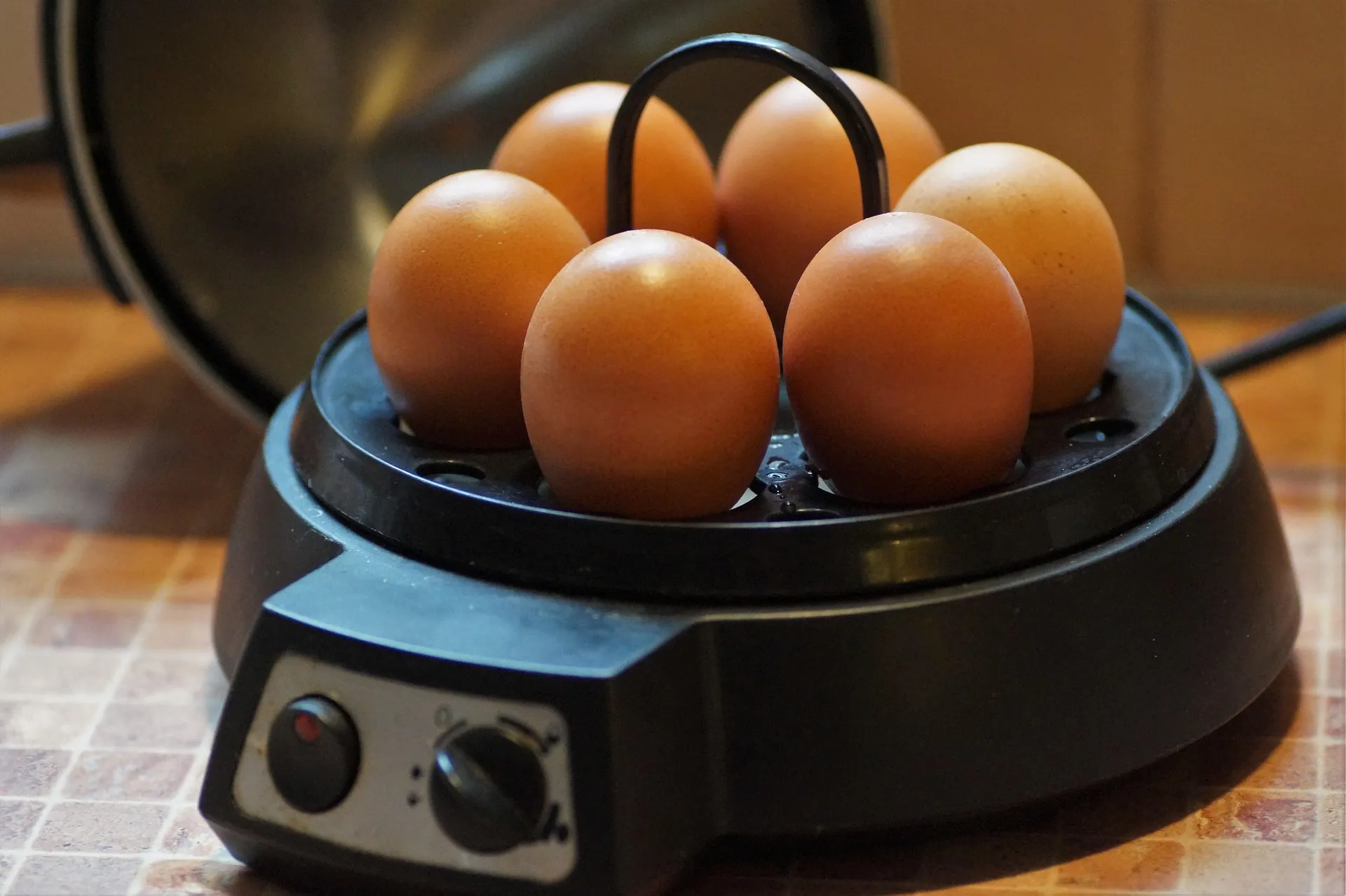 A black countertop electric cooker holding brown eggs on a tiled kitchen counter